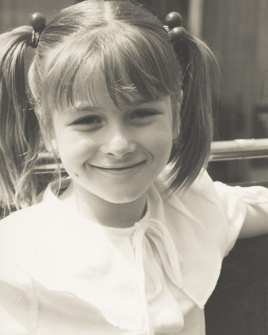 Emily as a little girl, grinning, with pigtails and a fringe